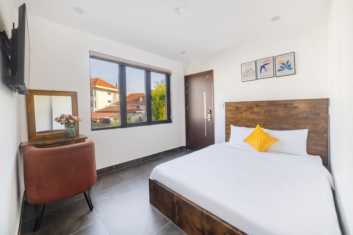 Ein Hotelzimmer mit Bett, Sessel, Fernseher, Fenster und Bildern an der Wand.