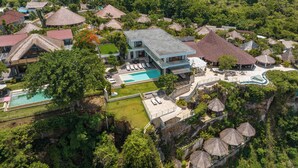 Vista aérea de um resort com vários edifícios de telhado de palha, uma piscina e vegetação exuberante.