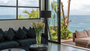 Uma sala de estar moderna com uma grande janela com vista para o oceano, um sofá, uma mesa de centro e uma luminária.