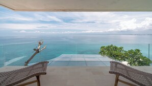 Varanda com vista para o mar, duas cadeiras de vime e grade de vidro.