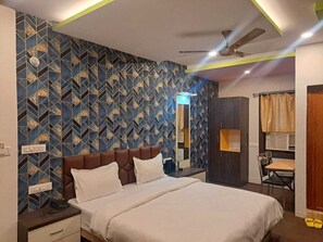 Quarto de hotel com cama, escrivaninha, cadeira, guarda-roupa e ventoinha no teto.