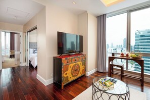 Habitación de hotel con un ventanal grande, un televisor en un mueble, una mesa de comedor con una cesta y una cama con vistas.