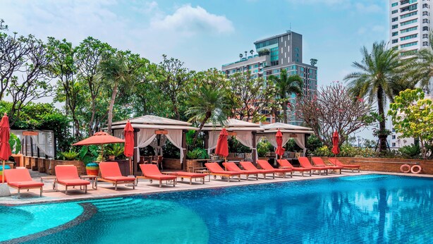 A swimming pool with lounge chairs and umbrellas, surrounded by greenery and modern buildings. - Serviced 2 Bed Superior Skyvillas - Check in From 15h to 22h Only (Bangkok)