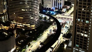 A nighttime cityscape with modern high-rise buildings, a curved road, and a bridge. - Serviced 2 Bed Superior Skyvillas - Check in From 15h to 22h Only (Bangkok)