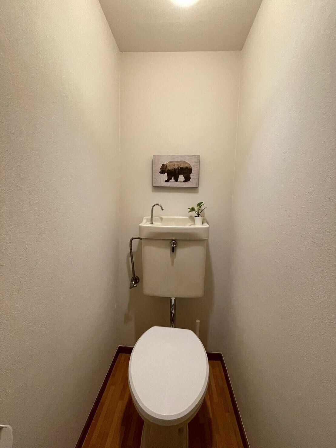A small bathroom with a toilet, sink, and a bear-themed wall decoration.