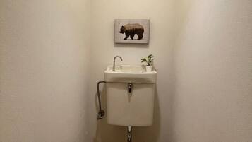 A small bathroom with a toilet, sink, and a bear-themed wall decoration.