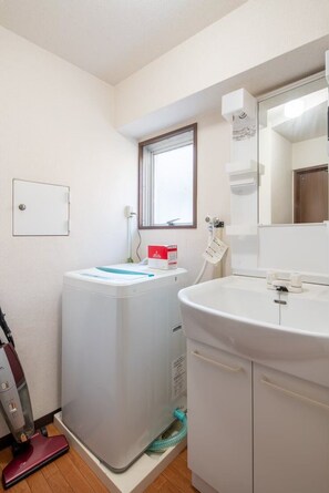 A compact bathroom with a washing machine, a vacuum cleaner, and a sink with a mirror. - Sunny heights 201 (Tokyo)