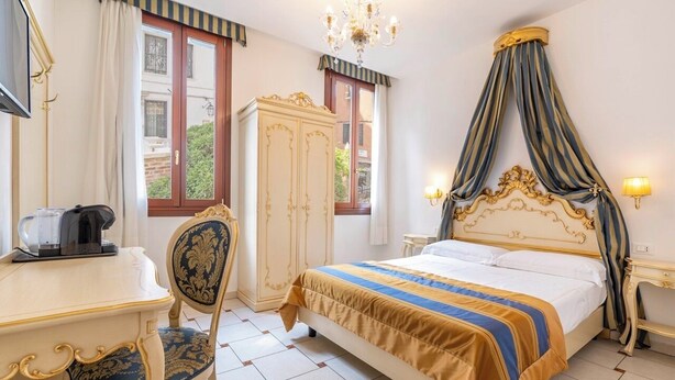 A hotel room with a bed, a desk, a chair, a wardrobe, and a chandelier. - Casa Marsilli (Venice)
