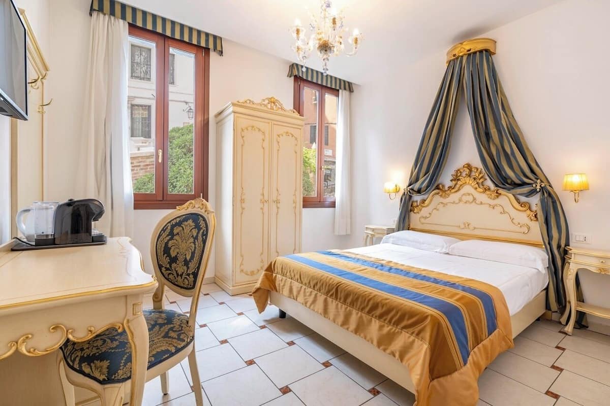 Una habitación de hotel con cama, escritorio, silla, armario y candelabro.