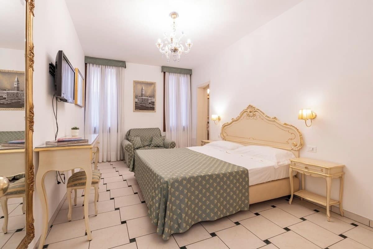 Una habitación de hotel con cama, escritorio, silla, televisor y candelabro.