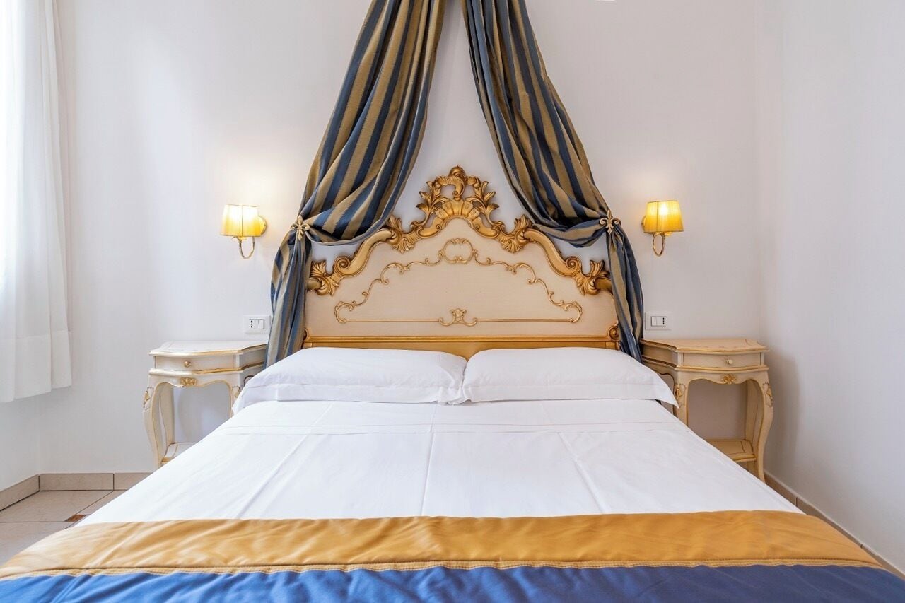 A bed with a gold ornate headboard, white bedding, and two bedside lamps.