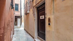 A narrow alleyway with a stone-paved path, a brown door with a lock, and a small sign on the wall. - Casa Marsilli (Venice)