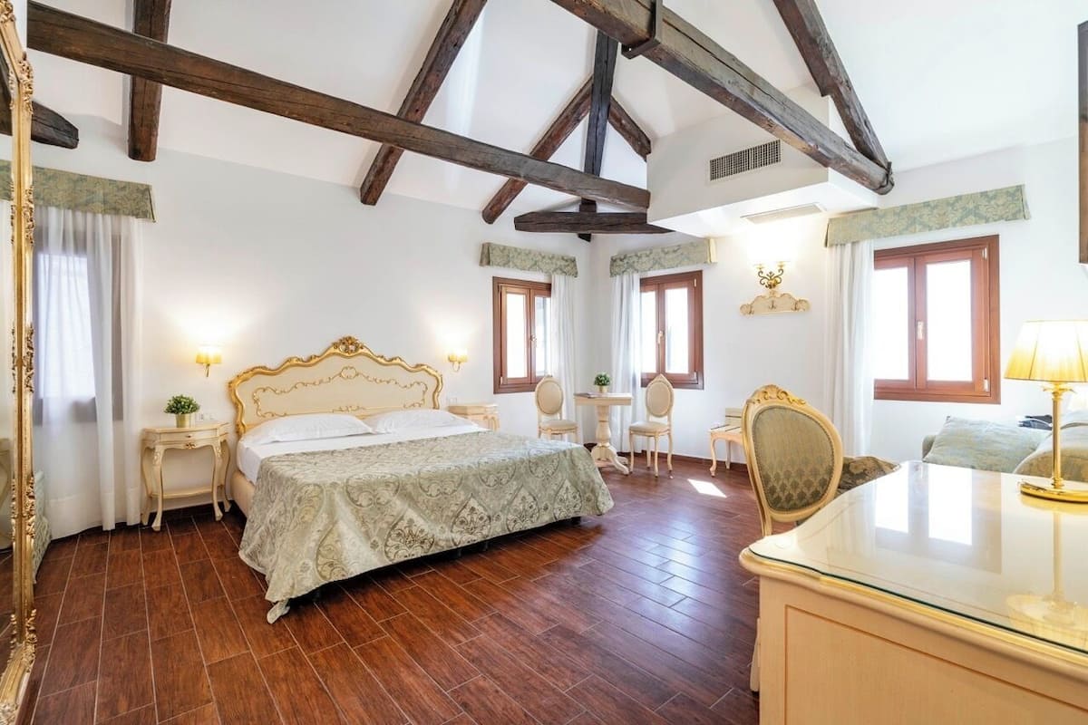 Un dormitorio con una cama grande, un escritorio, dos sillas y un espejo.