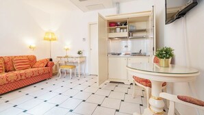 A compact living space with a sofa, a small table, a desk, a kitchen area, and a TV mounted on the wall. - Casa Marsilli (Venice)