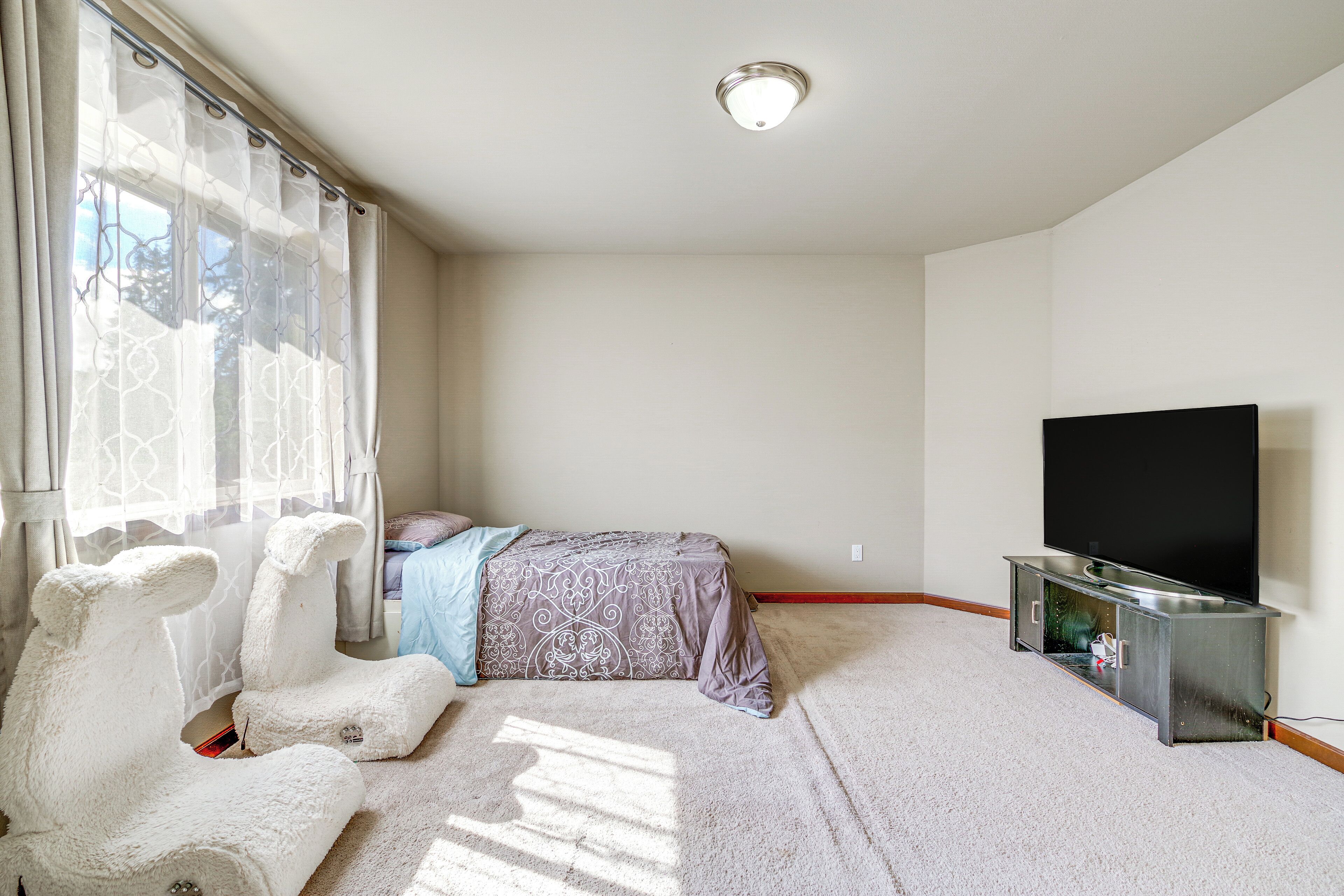 A bedroom with a bed, a TV, and a window with curtains.