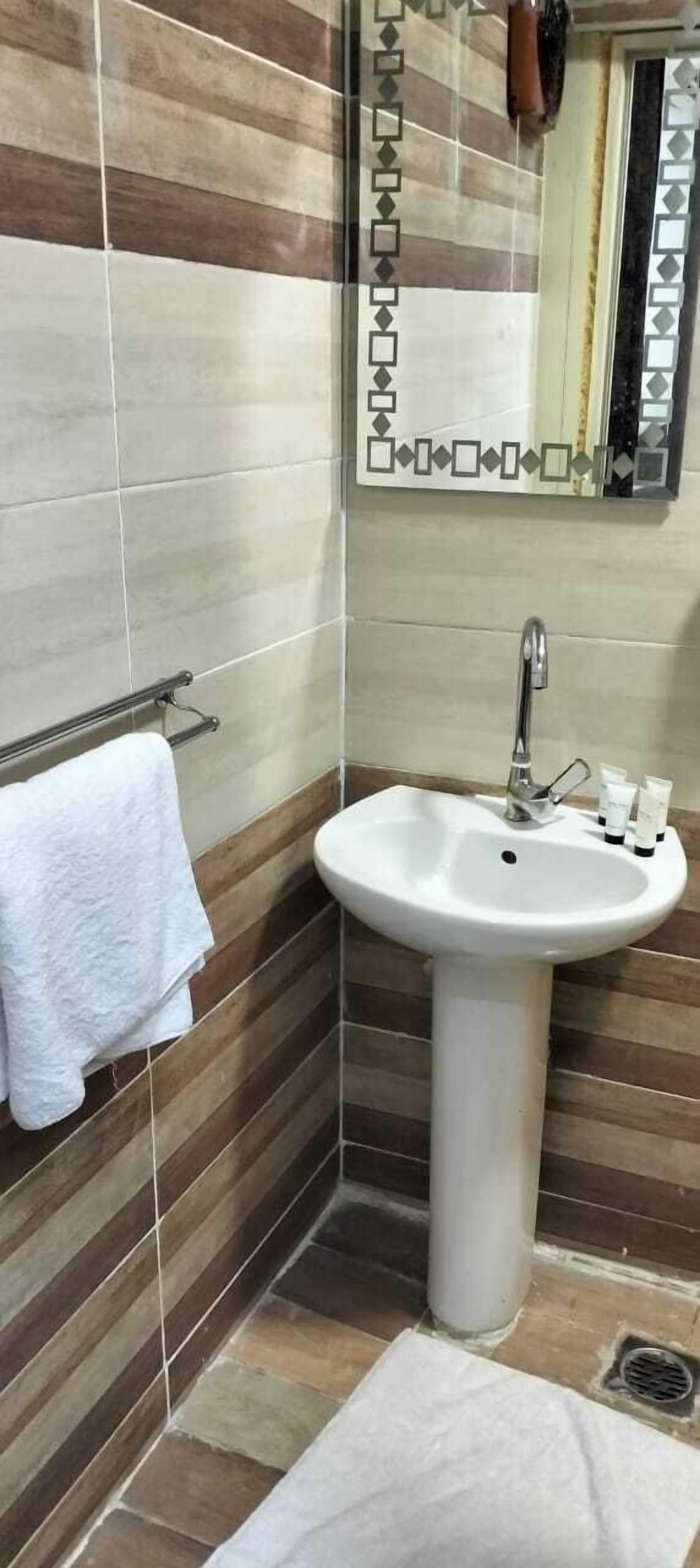 Une salle de bain avec un lavabo blanc, un porte-serviettes et un miroir orné d’un cadre décoratif.
