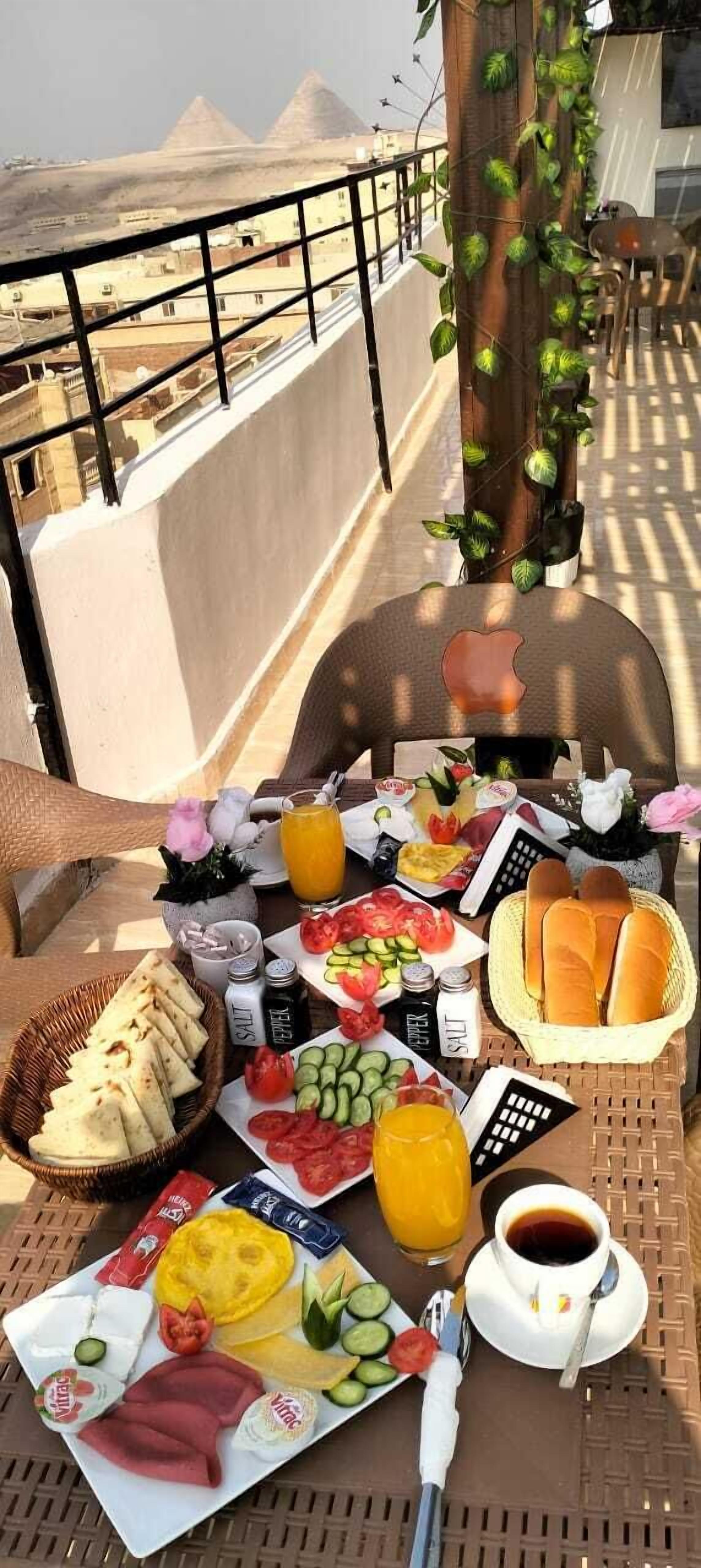 Desayuno en un balcón con vistas a las pirámides, que incluye pan, huevos, verduras y bebidas.
