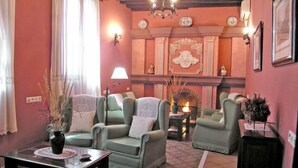 A cozy living room with a fireplace, green armchairs, and a table with a vase. - Hotel La Casa Grande del Burgo (El Burgo)
