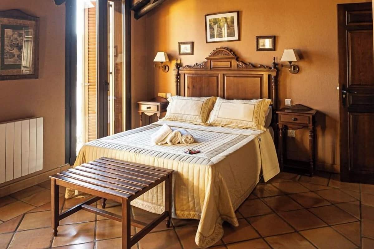 Een slaapkamer met een houten plafond, een bed met houten hoofdbord, een bankje en betegelde vloer.
