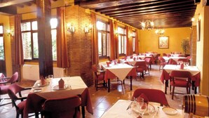 A restaurant with wooden beams, brick walls, and red chairs. Tables are set with white tablecloths and red napkins. - Hotel La Casa Grande del Burgo (El Burgo)
