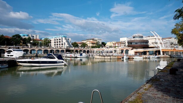 Ein Yachthafen mit vertäuten Booten, einer Brücke und Gebäuden im Hintergrund.