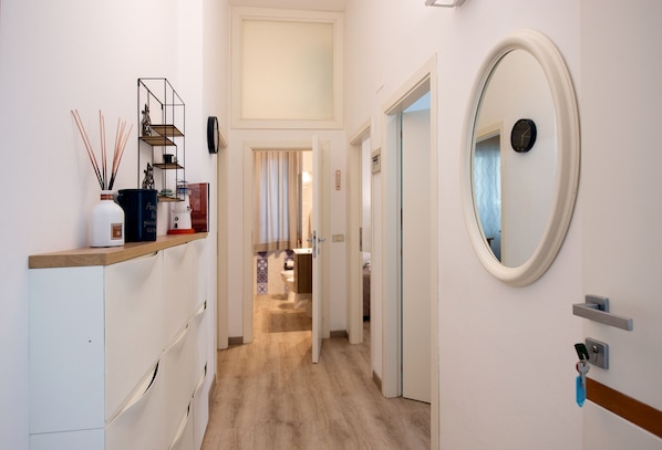 A hotel hallway with a wooden floor, white walls, a mirror, and a shelf with decorative items. - Frog 30 in Gabicce Mare (Gabicce Mare)