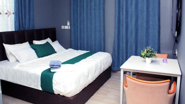 Een hotelkamer met een bed, een bureau, een stoel, een potplant en blauwe gordijnen.