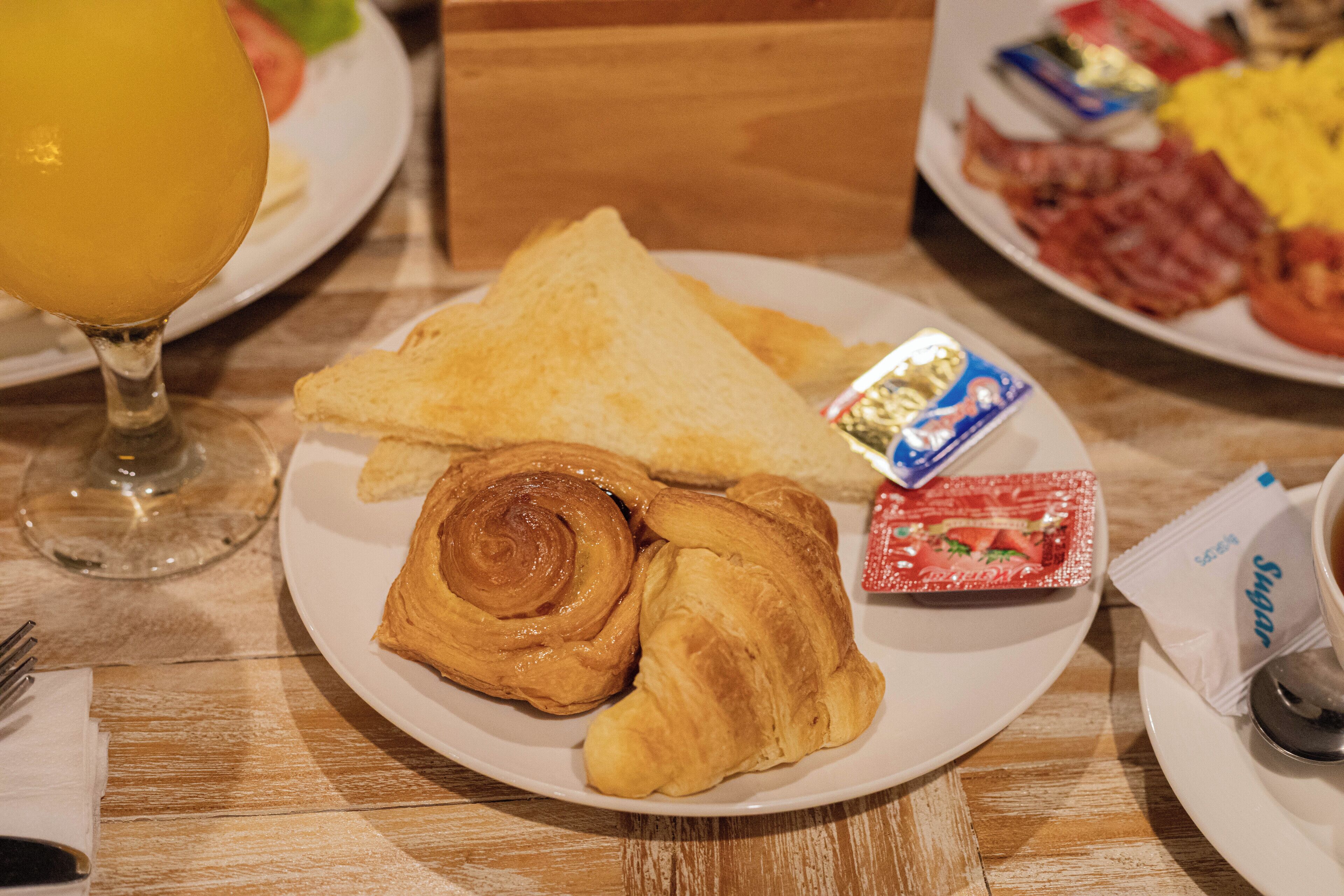 A breakfast plate with croissants, a glass of orange juice, and a packet of sugar.