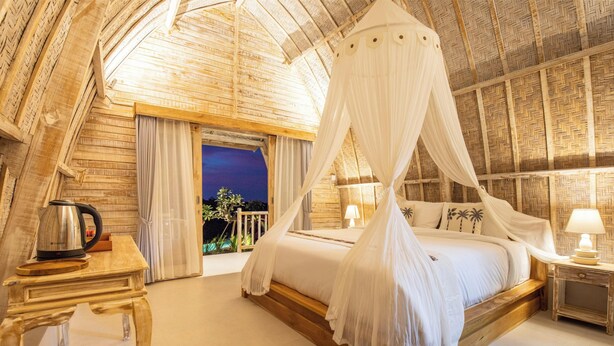 A bedroom with a canopy bed, wooden walls, a nightstand, and a view of the outside. - Wijaya Cottage Nusa Penida (Penida Island)