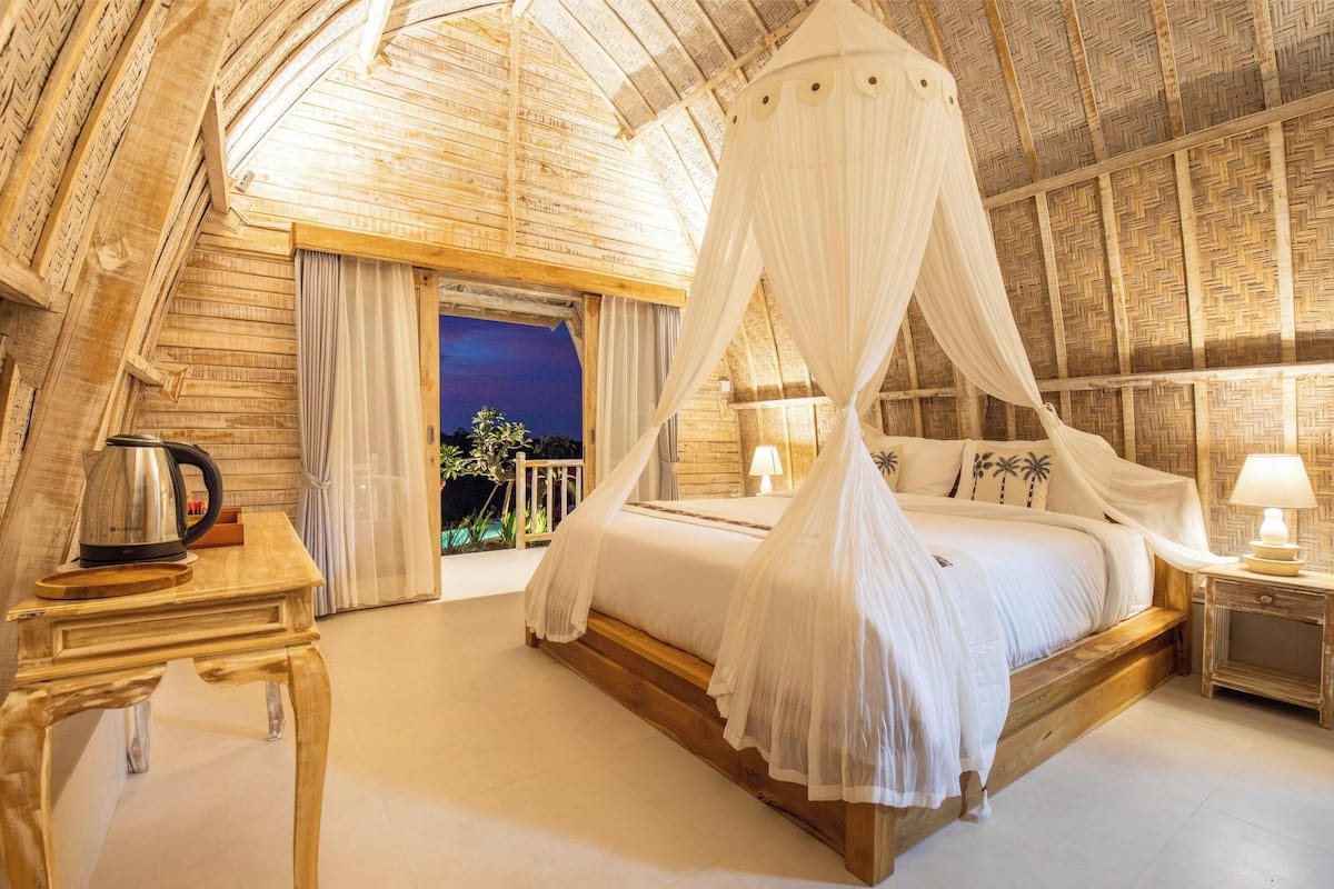 A bedroom with a canopy bed, wooden walls, a nightstand, and a view of the outside.