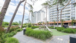 A modern apartment building with a rooftop garden, a children's play area, and a parking lot.