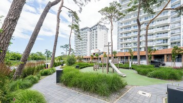 Un moderno edificio de apartamentos con jardín en la azotea, zona de juegos para niños y aparcamiento.