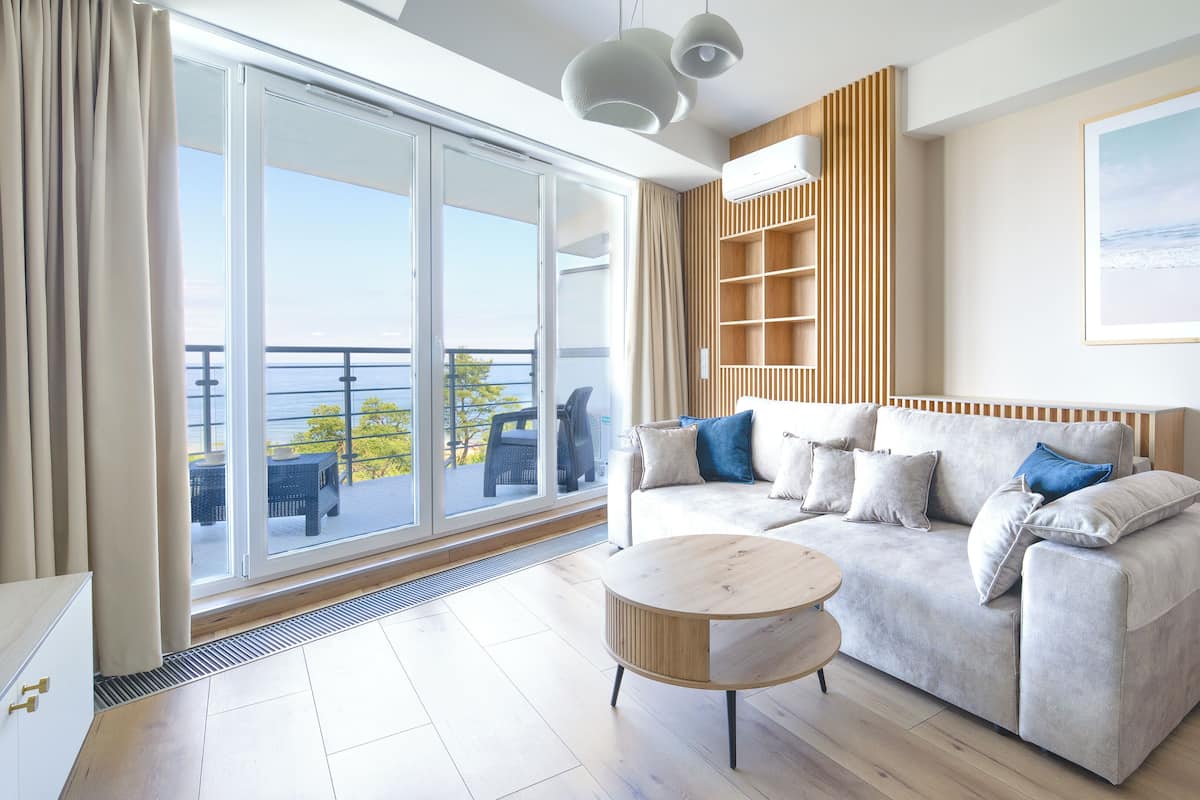 A modern living room with a sofa, a coffee table, and a view of the sea through large windows.