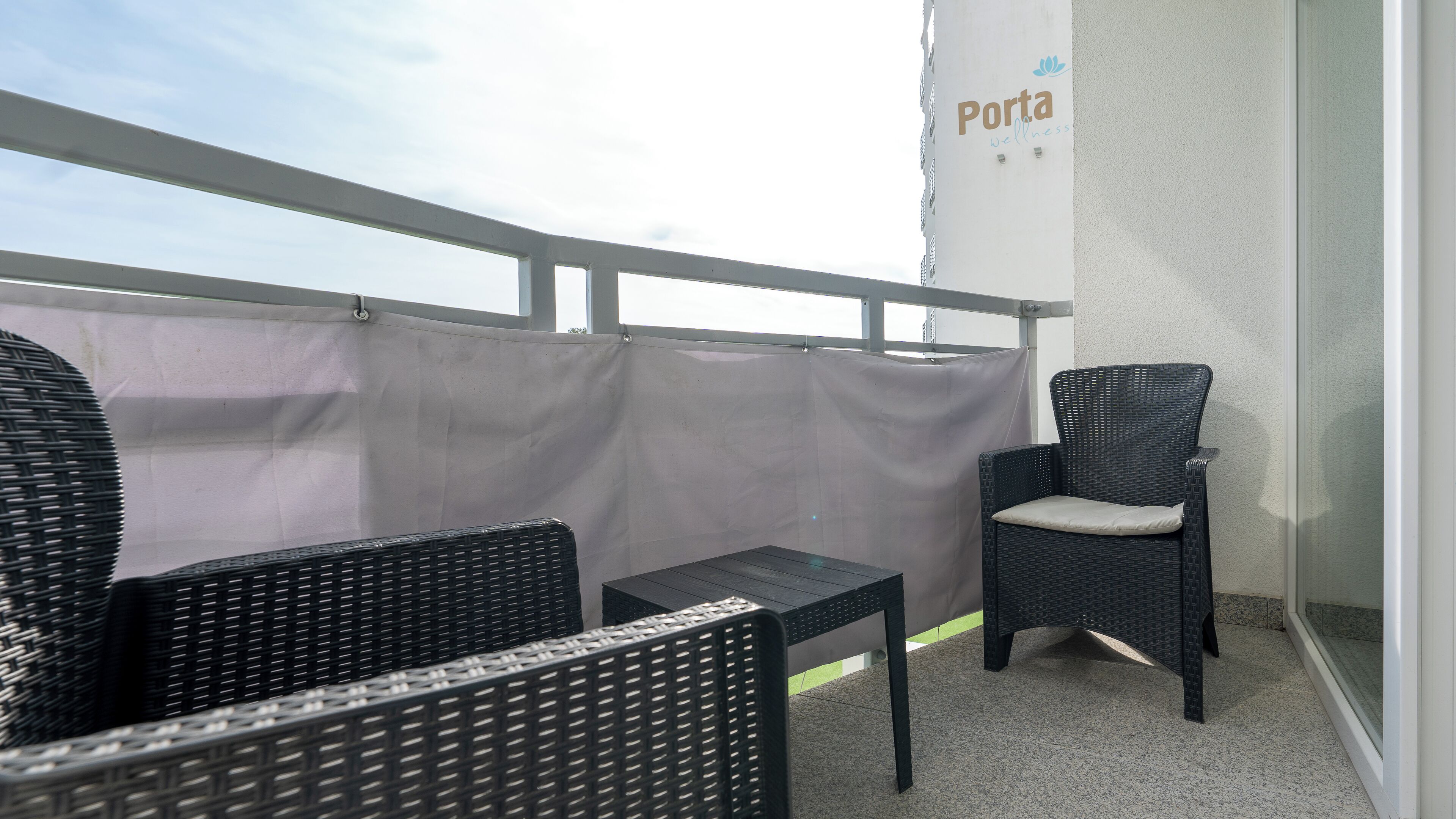 A balcony with wicker furniture, a grey curtain, and a wall with 'Porta Wellness' signage.