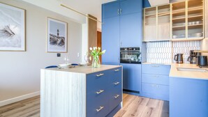 A modern kitchen with blue cabinets, a wooden countertop, and a dining area with a white table and chairs.