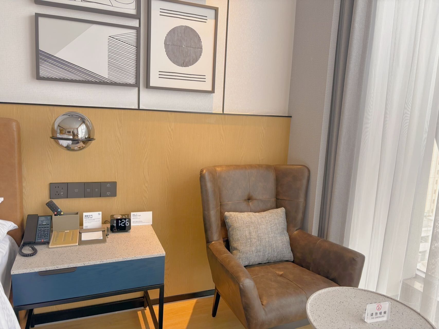 A hotel room with a desk, chair, and a small table with a 'No Smoking' sign.