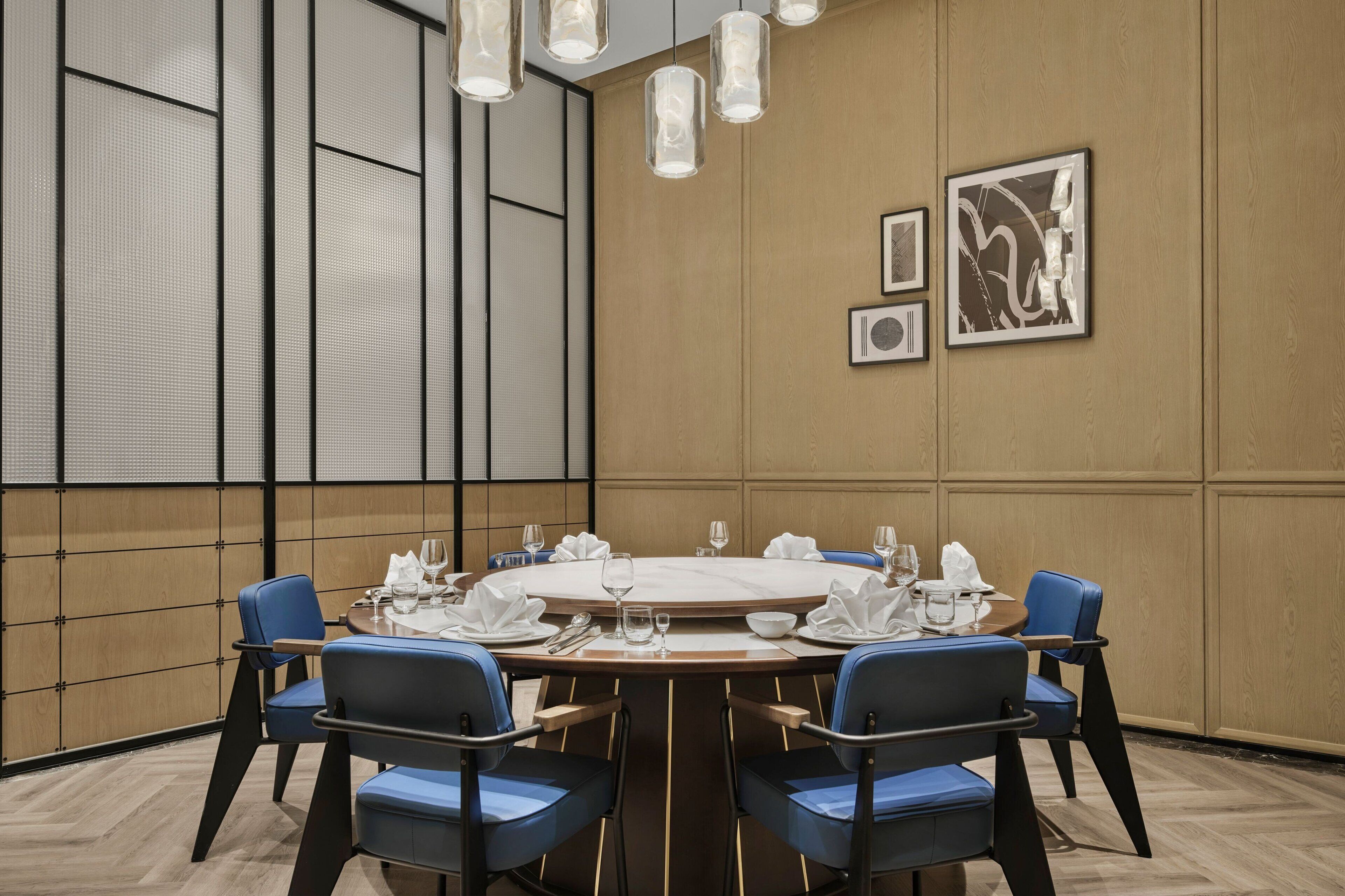 A conference room with a round table, blue chairs, and framed artwork on the wall.