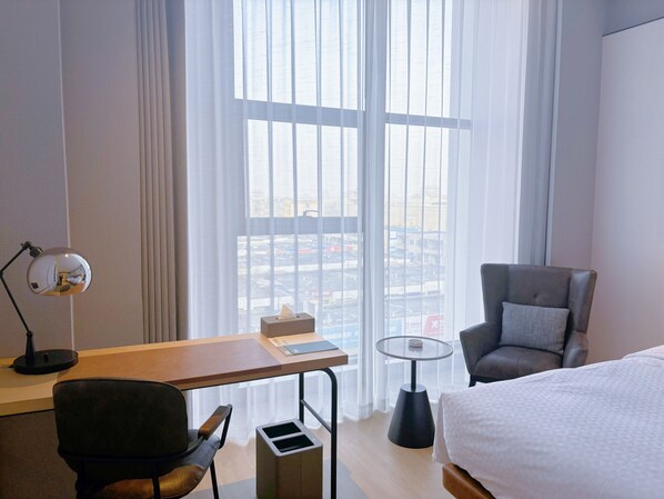 A hotel room with a bed, a desk with a lamp, a chair, a small table, and a window with a view of buildings. - Four Points Datong Pingcheng (Datong)