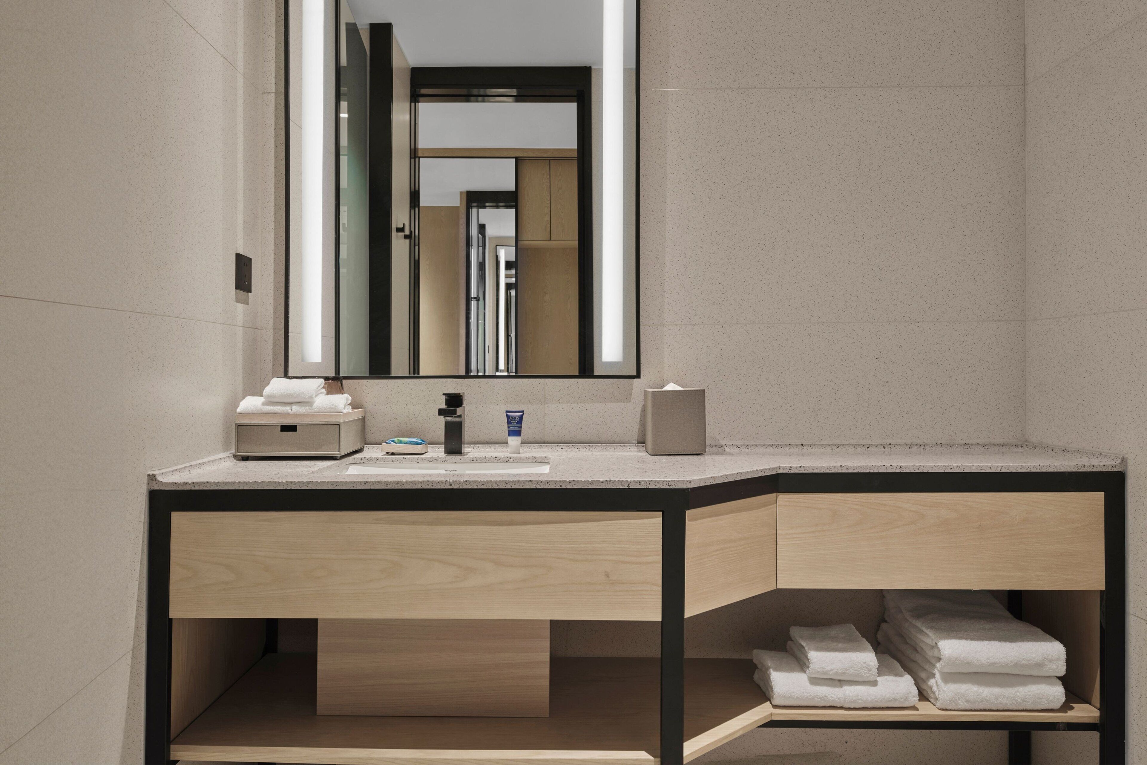 A modern bathroom with a wooden vanity, a mirror, and a towel rack.