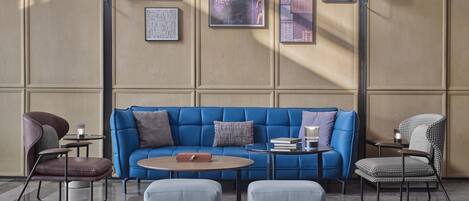 A modern lounge area with a blue sofa, two armchairs, a coffee table, and a small side table.