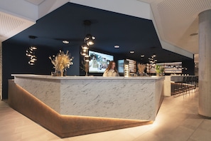 A modern reception desk with a marble top, a woman standing behind it, and a large screen displaying content.