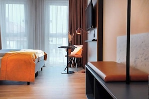 A hotel room with a bed, a sofa, a TV, and a small table with a chair.