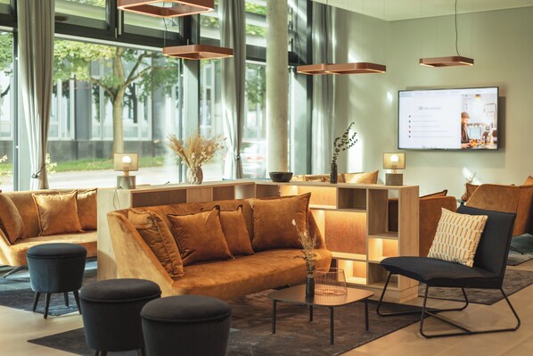 A modern lobby with a sofa, chairs, a coffee table, and a TV screen.