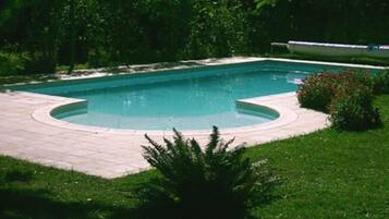 A rectangular swimming pool with a tiled deck, surrounded by grass and trees.