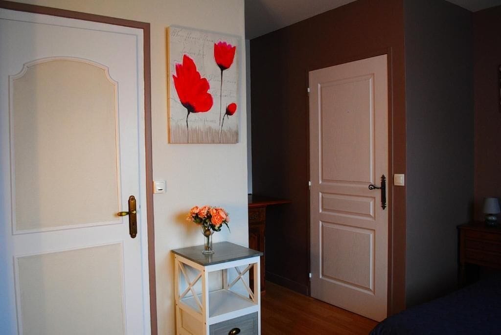 Una stanza con una porta bianca, un tavolino con un vaso di fiori e un dipinto di fiori rossi al muro.