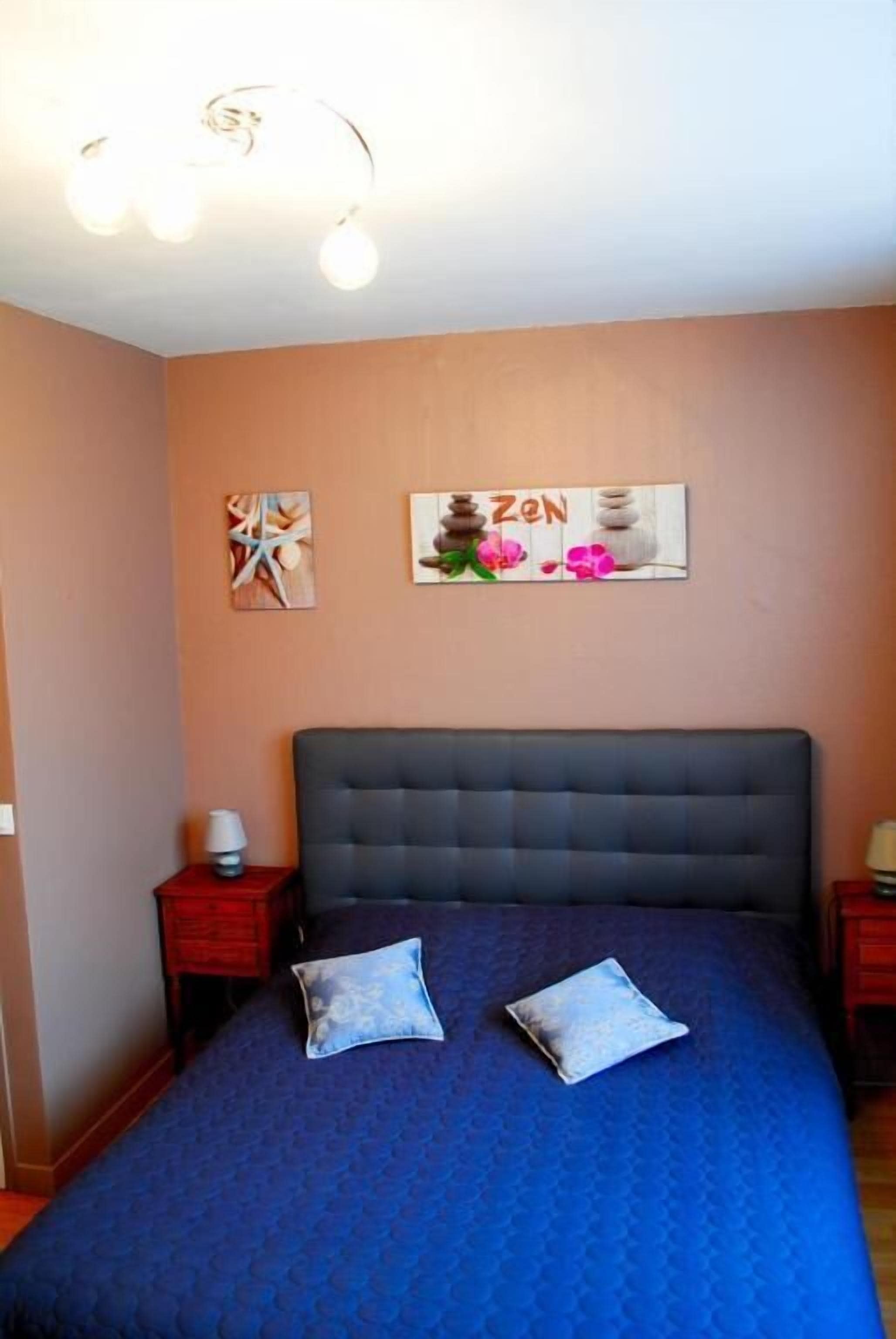 Une chambre à coucher avec un grand lit, deux oreillers, une table de chevet avec une lampe et des œuvres d’art murales.