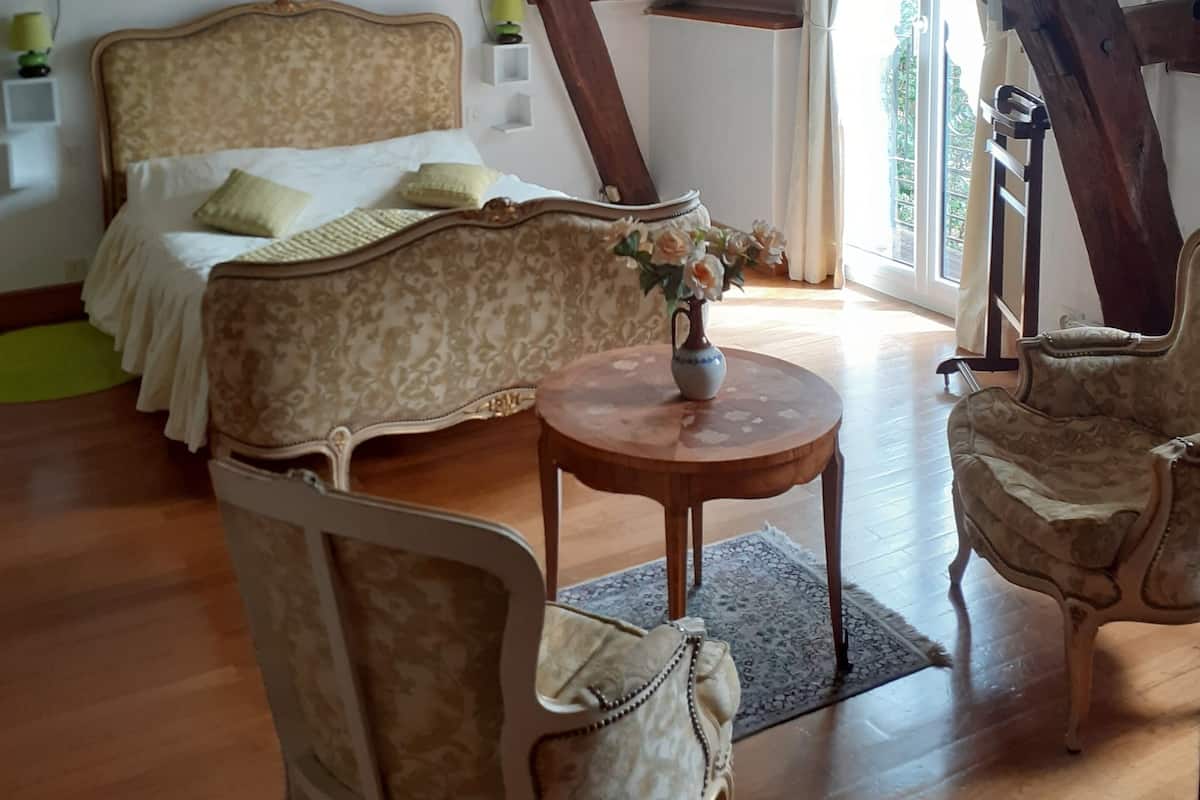 Quarto com cama, uma mesinha com um vaso, duas cadeiras e estrutura de teto de madeira.