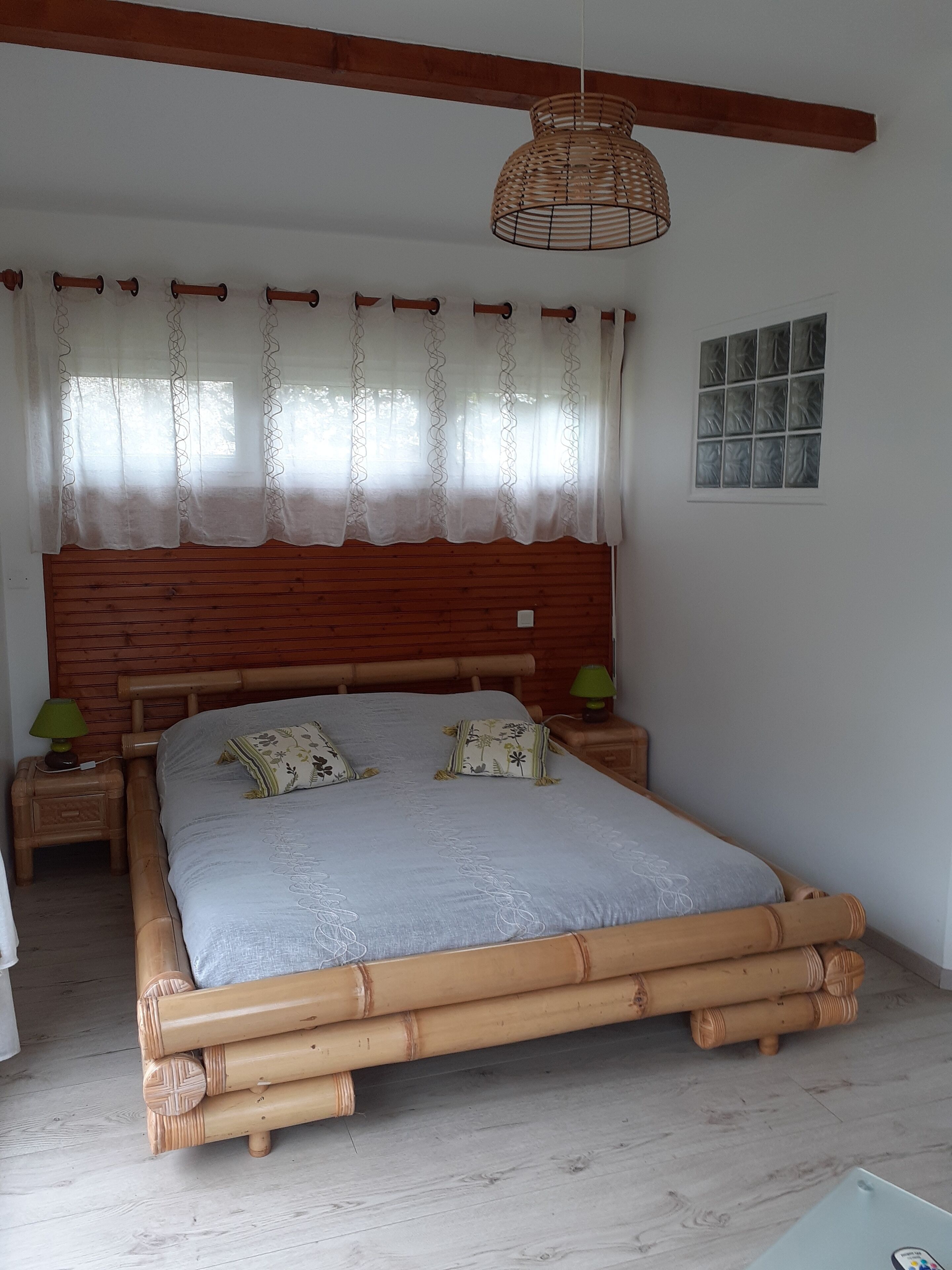 A room with a wooden bed frame, a large window with curtains, a bedside lamp, and a wall-mounted light fixture.
