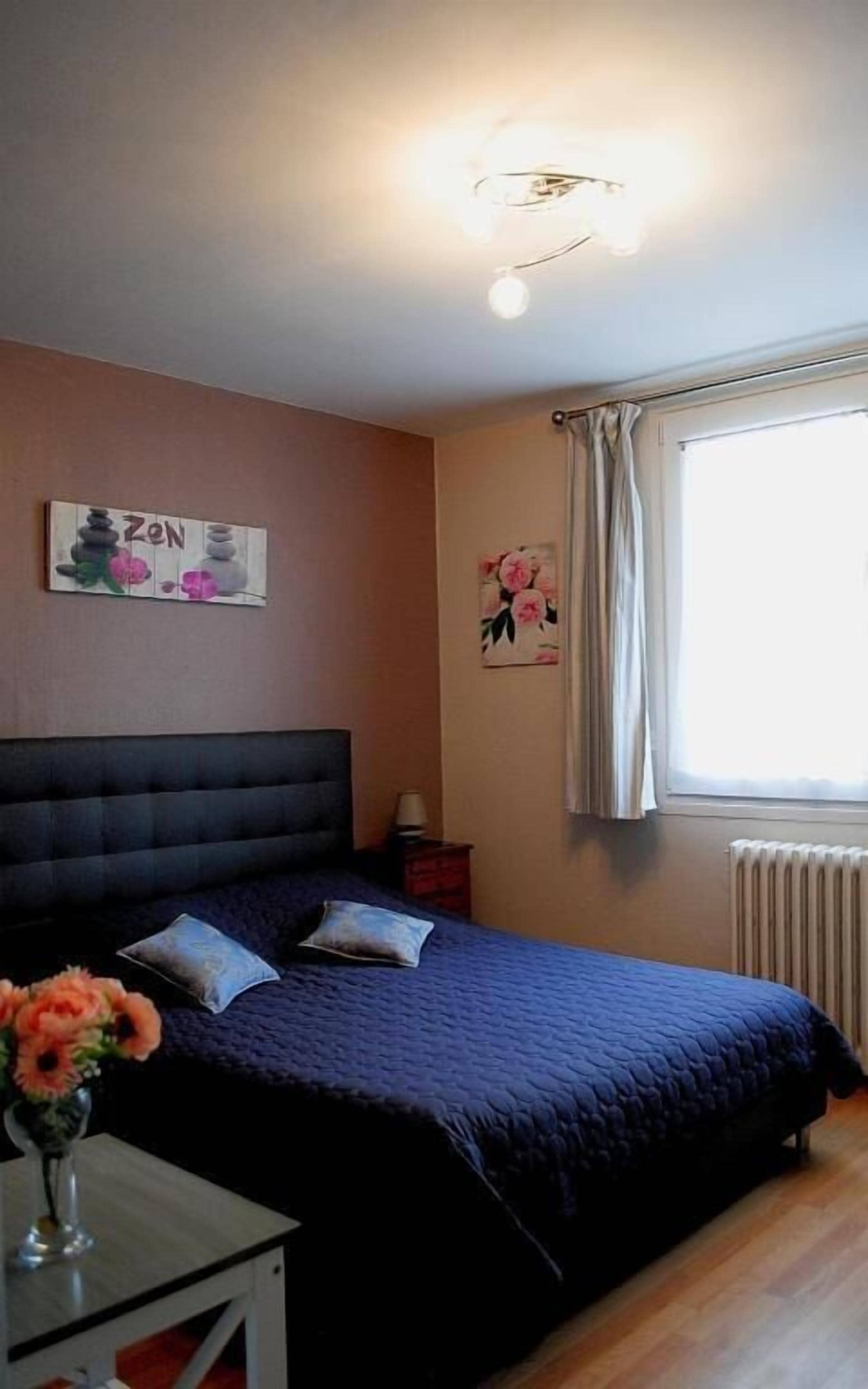 Une chambre à coucher avec un lit, une table de chevet, une lampe, un vase avec des fleurs et un tableau au mur.