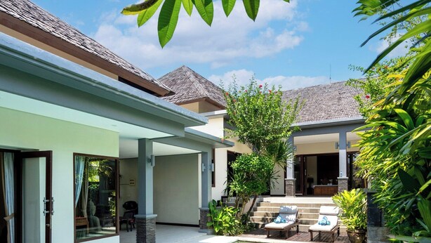 A swimming pool with clear blue water, surrounded by a house with a tiled roof, and lush greenery. - Senang Villa by Betterplace (Canggu)